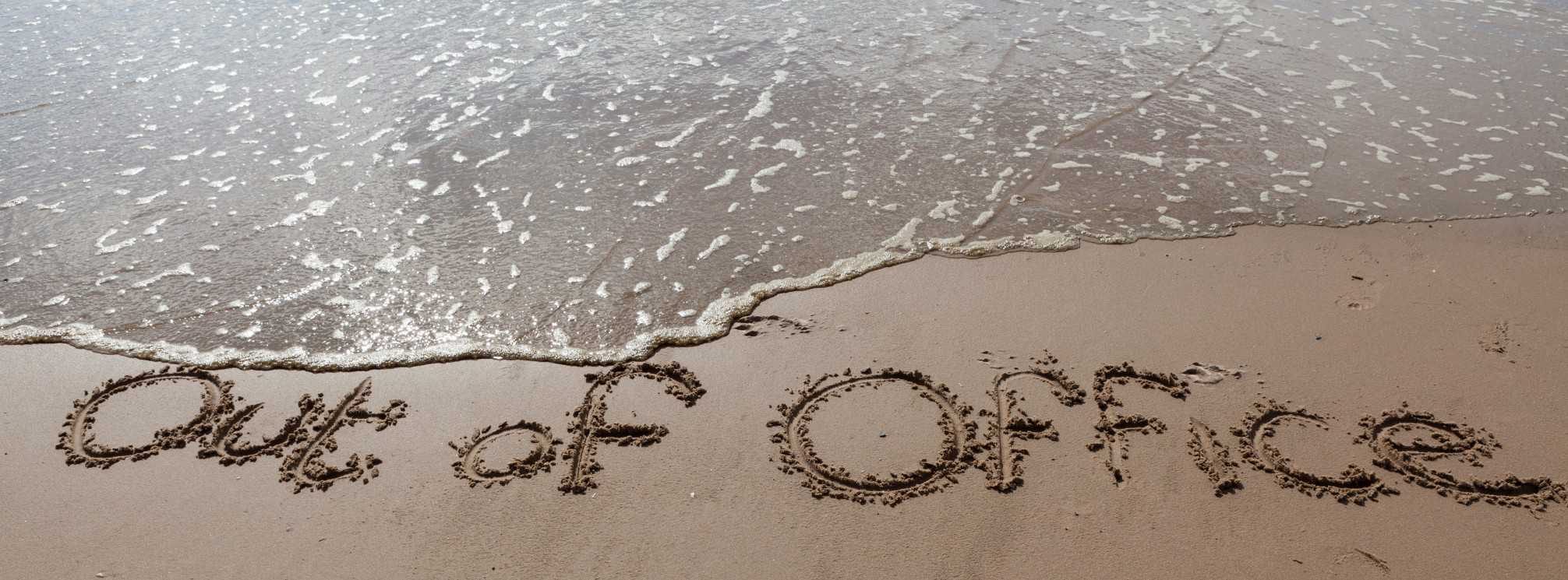out of office written in the sand of a beach