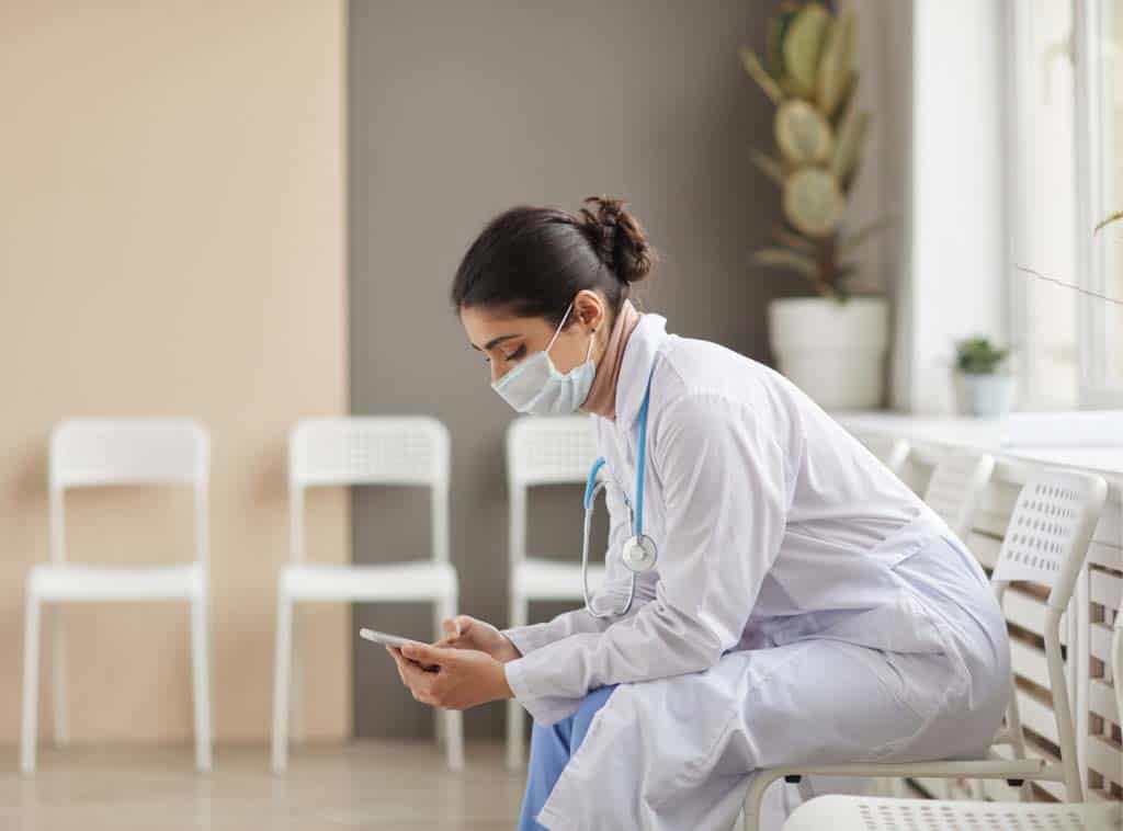 female doctor wearing a face covering uses her mobile phone