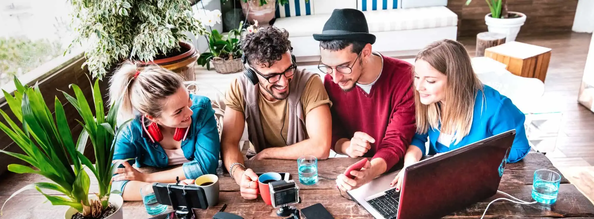 a group of four generation z people in the workplace crowded around a laptop and someone showing something on their iPhone