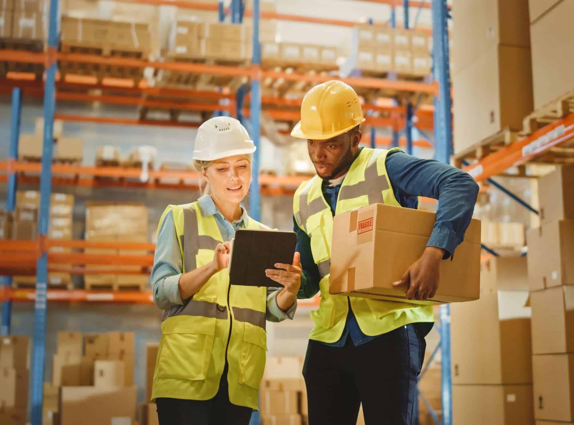 male and female warehouse employee talking and looking at an ipad