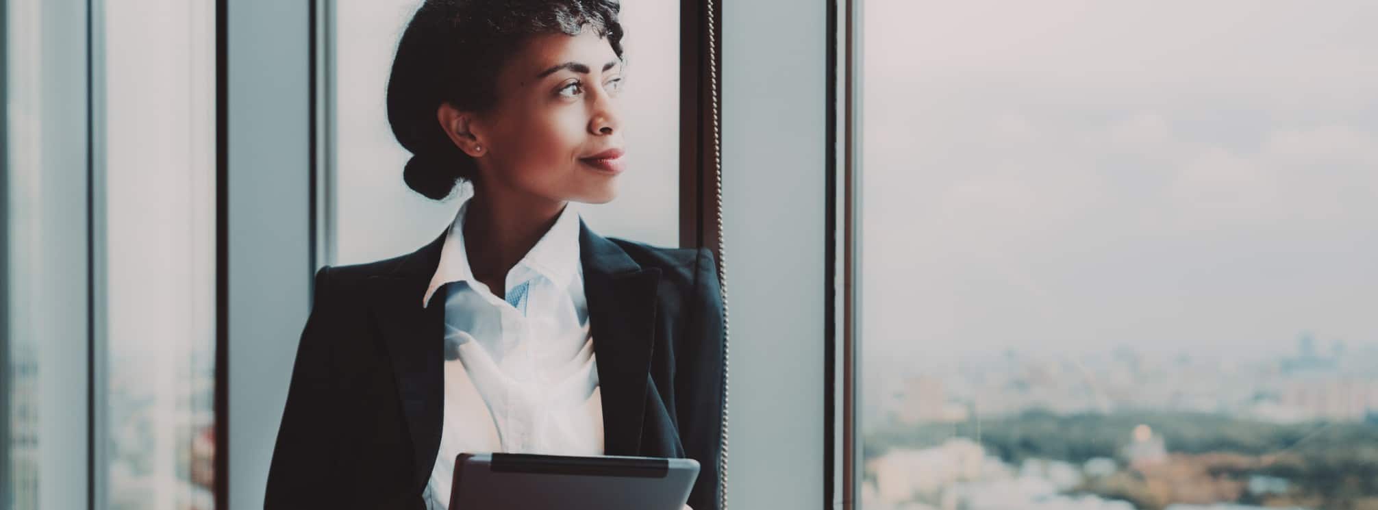 black female CEO looking out her window and holding a tablet