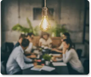 illuminated lightbulb hanging above a table of professionals working on an internal communication strategy