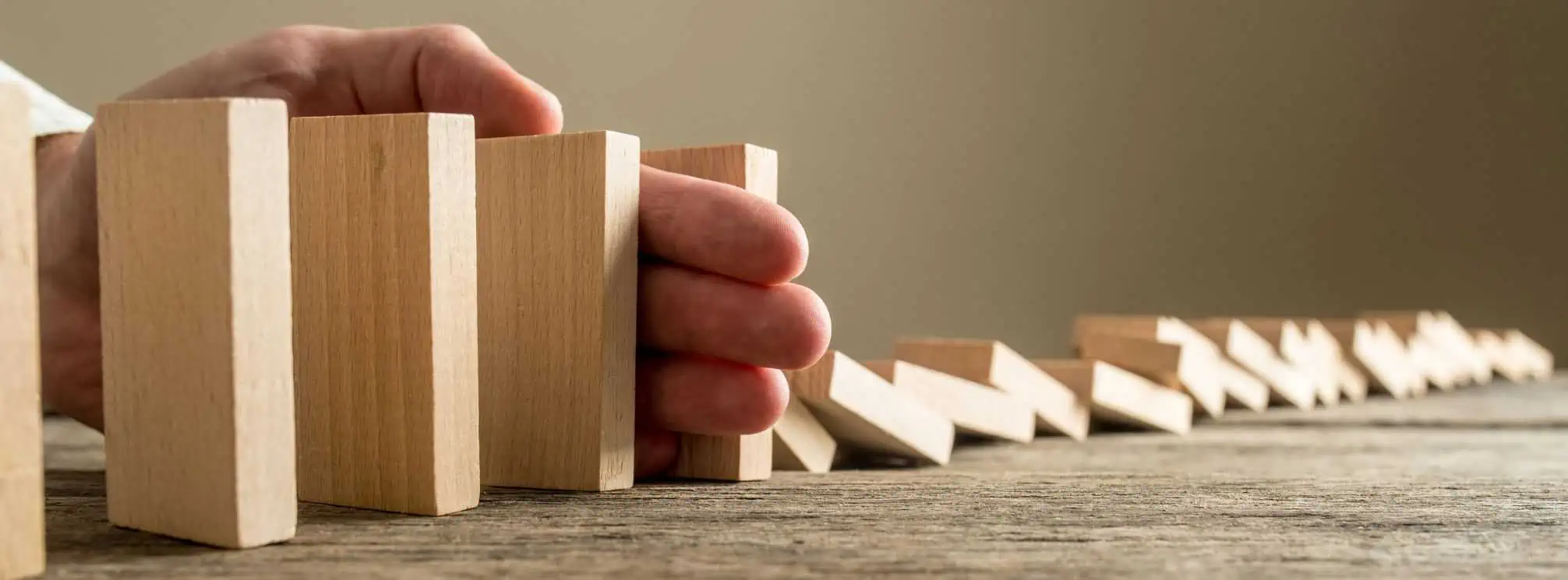 man's hand stopping dominoes from toppling over the rest of the dominoes in a line