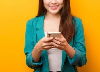 Asian woman smiling and using her phone to text. This represents texting for business communication.