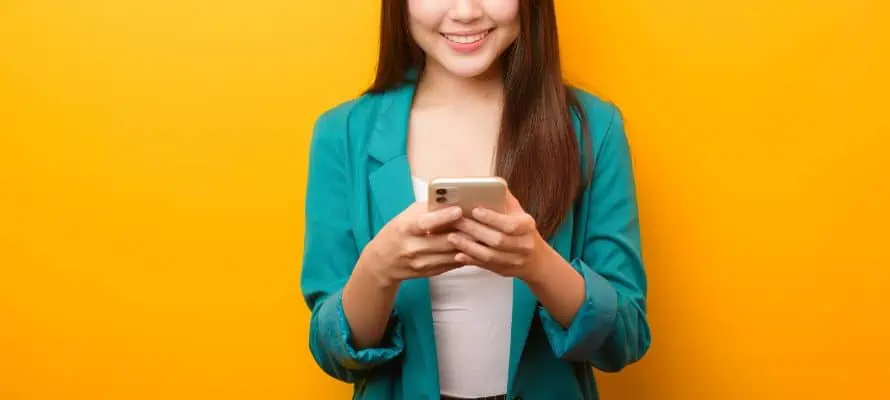 Asian woman smiling and using her phone to text. This represents texting for business communication.