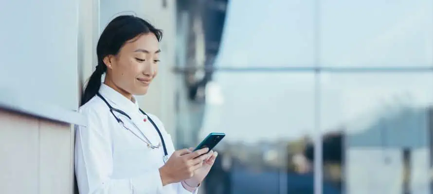 female physician on a break outside the hospital, checking her smartphone