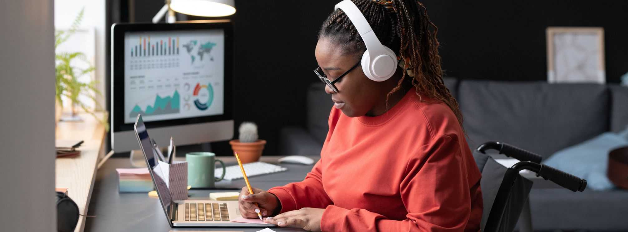 young black woman working at her desk in her home office. Remote worker listening to Beats.