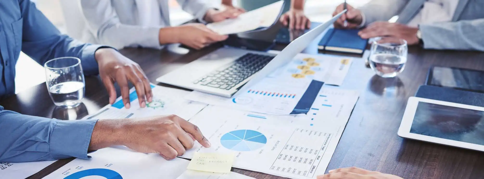 table full of papers with charts and data visualizations on them with the hands of professionals pointing to certain reports