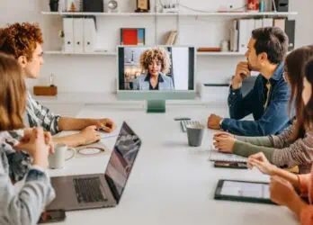 engaged hybrid employees in the workplace, with five in person staff and one remote dialed in on the computer