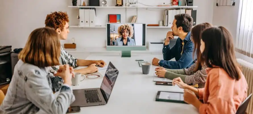 engaged hybrid employees in the workplace, with five in person staff and one remote dialed in on the computer