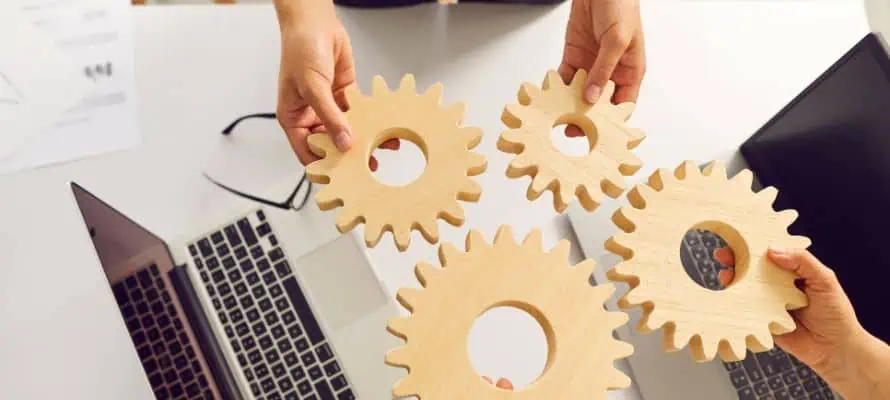 two professionals holding wooden gears close together to represent finding hybrid workforce solutions