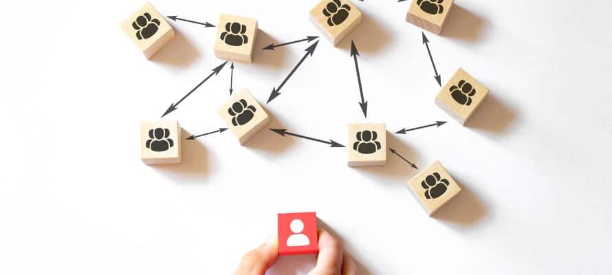 one red block with a person icon to represent a manager with a bunch of other wooden blocks with people icons all interconnected. This represents managing a hybrid workforce.