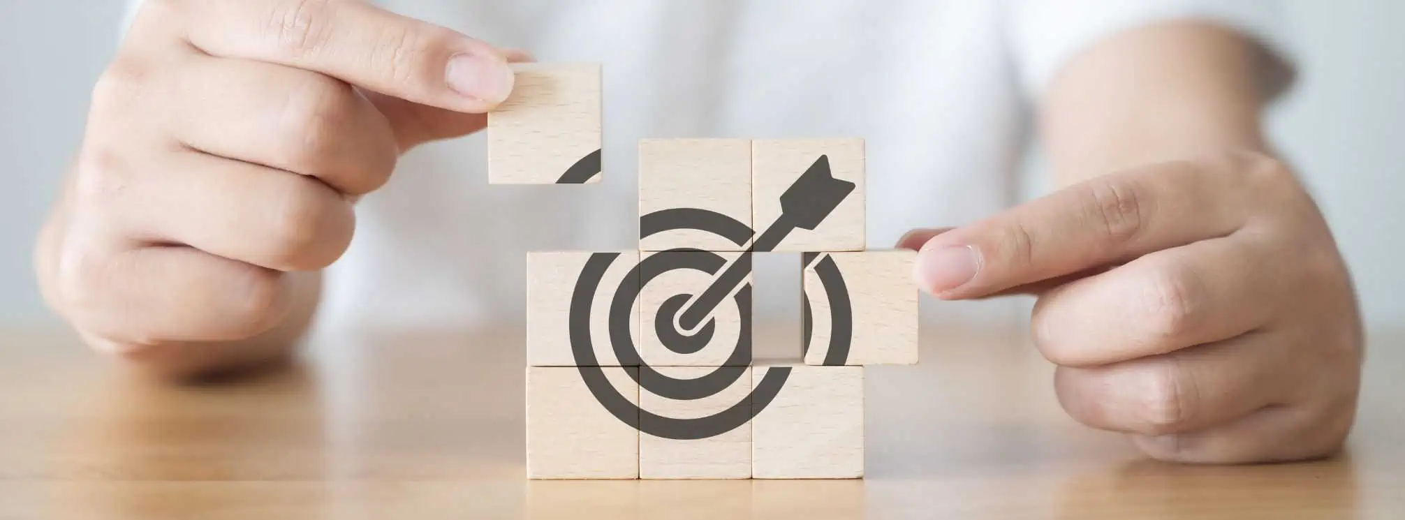 woman putting together a grid of wooden blocks to make up an icon of an arrow hitting a target