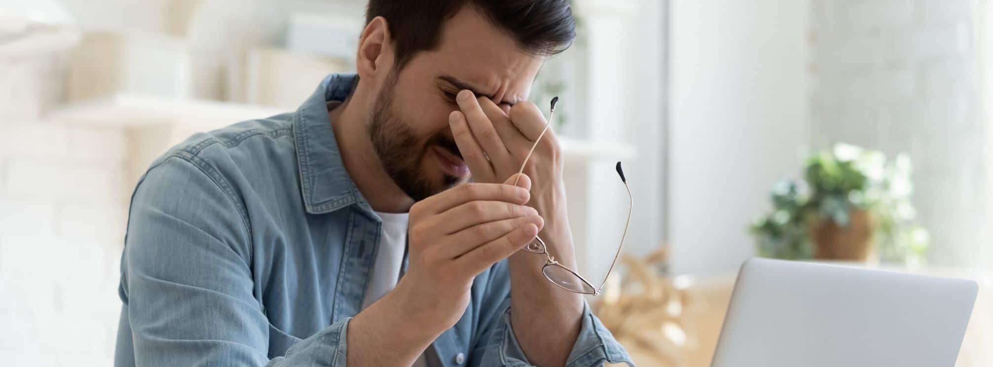 survey fatigue depiction. Man working at his computer with his glasses pulled off and rubbing his eyes.