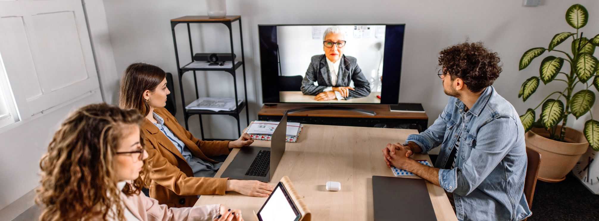 photo example of a hybrid workforce where one remote employee is dialed into a meeting on a tv screen and the other three employees are in the office
