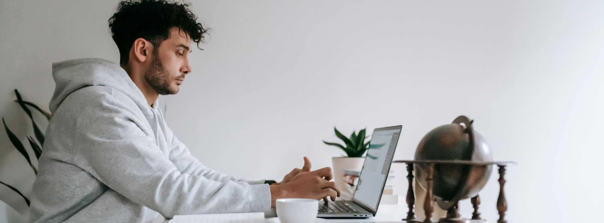 photo of a male remote employee working on his laptop in his home office, wearing a sweatshirt 