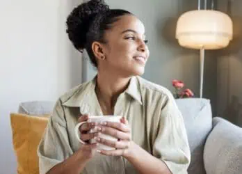 Smiling happy woman drinking her morning coffee and looking out the window