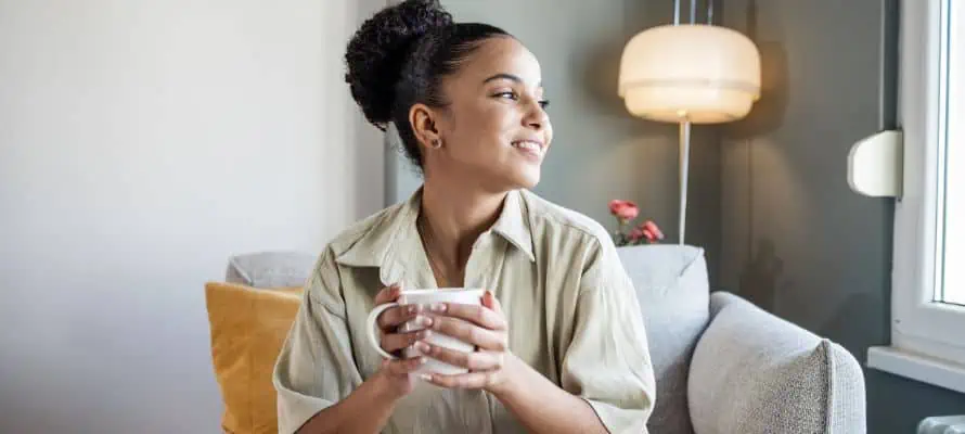 Smiling happy woman drinking her morning coffee and looking out the window