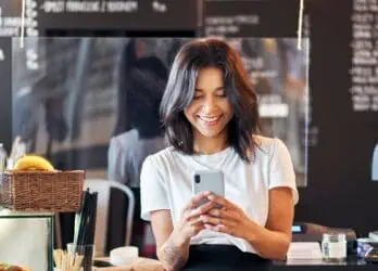 example of text messaging for businesses. Young female employee texting in front of the cash register in a casual restaurant.