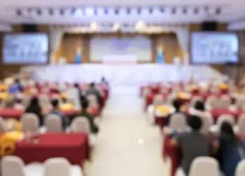 Company town hall meeting being held in person with seating and a stage with a blur effect on the picture.