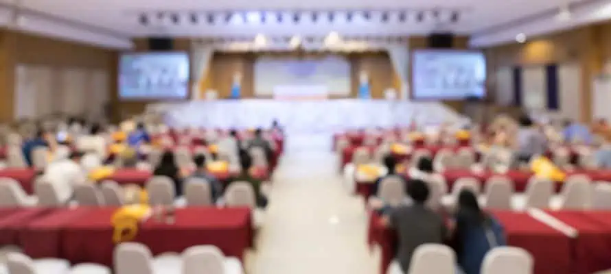 Company town hall meeting being held in person with seating and a stage with a blur effect on the picture.