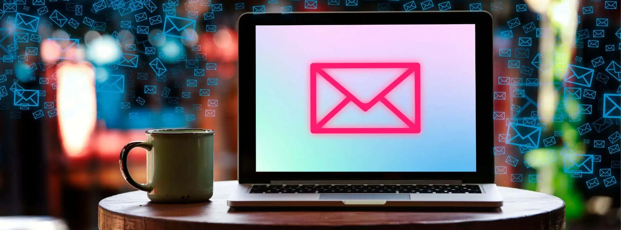 Open laptop on a table with a multi-color graphic on the screen of a mail icon. Cup of coffee on the table beside the laptop.