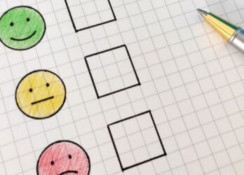 Employee pulse survey on paper with a green, yellow, and red smiley face with check boxes beside them and a pen resting on the paper