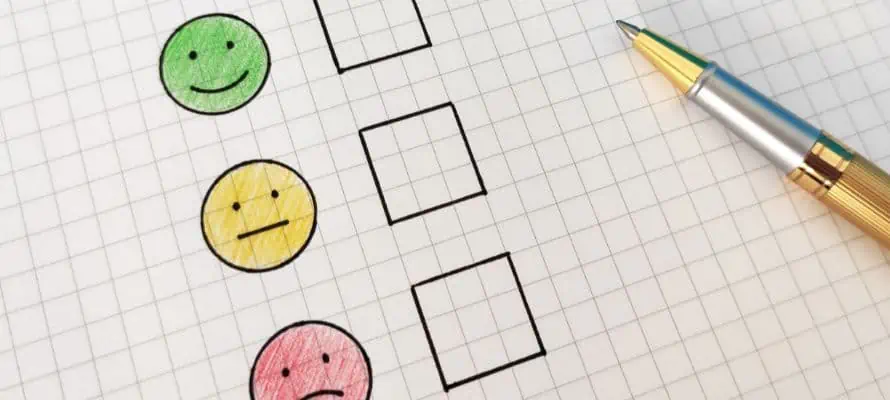 Employee pulse survey on paper with a green, yellow, and red smiley face with check boxes beside them and a pen resting on the paper