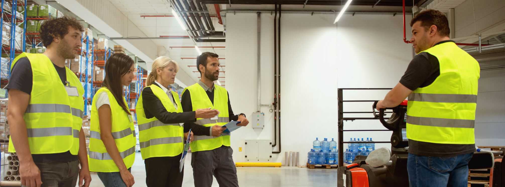 Logistics employees in safety vests watching a safety demonstration for warehouse equipment