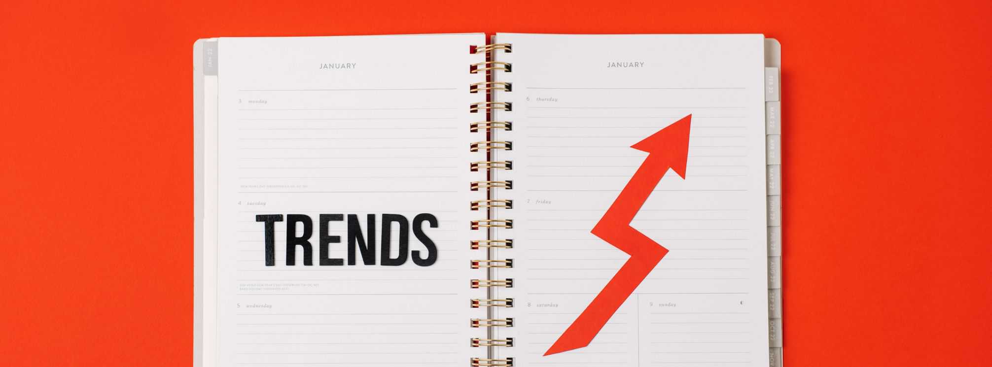 Red background with a notebook on it that says trends with an arrow pointing up