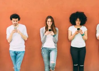 Group of five people leaning against an orange wall and texting. This is to represent sending mass texts to employees.