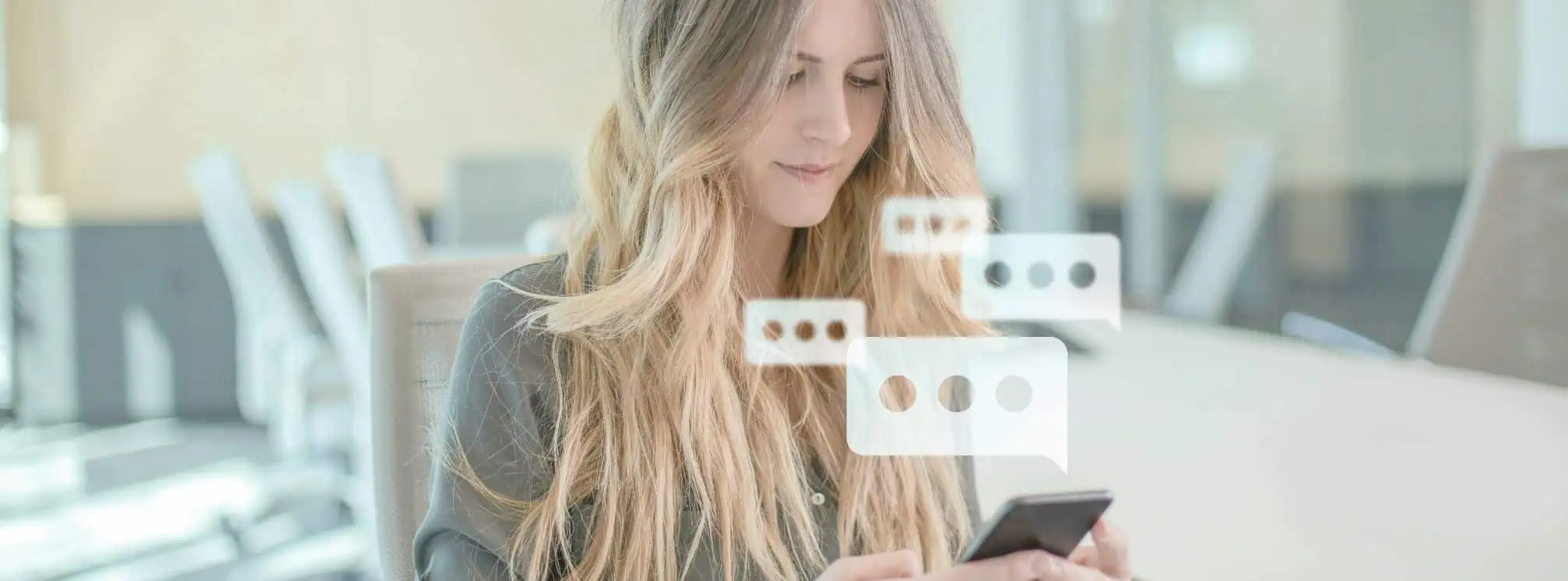 Female employee sitting at her desk and receiving text messages on her phone.