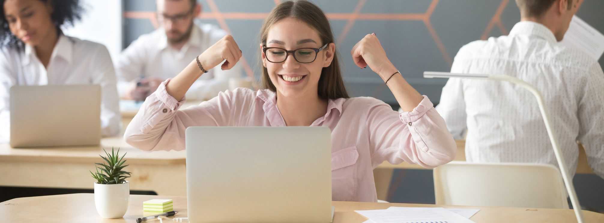 Motivated and engaged employee celebrating at her desk with her laptop open in front of her