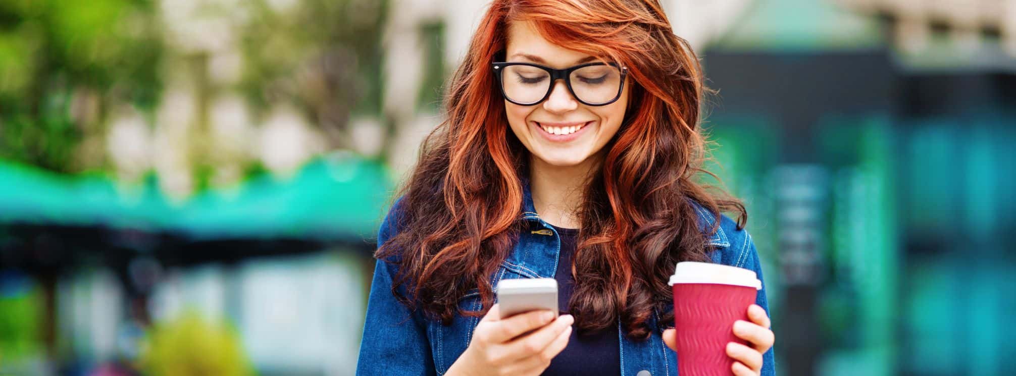 Red haired woman drinking a coffee and checking her phone on the way to work
