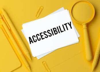 Yellow background with office supplies in the same yellow color with white notecards in the center with the word "accessibility" written on them.