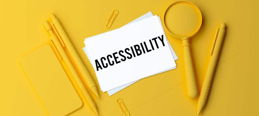 Yellow background with office supplies in the same yellow color with white notecards in the center with the word "accessibility" written on them.