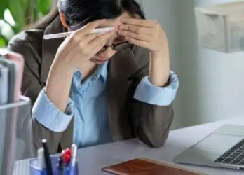 Disengaged employee sitting at her desk with her head in her hands, not working.