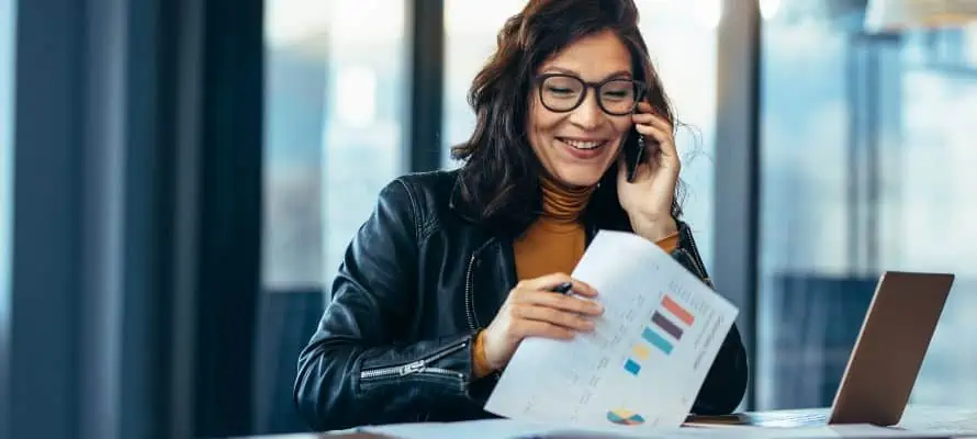 Female professional going through a stack of data on her desk, while talking on her cellphone.