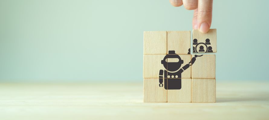 3 by 3 stack of wooden blocks with a design of a robot holding a magnifying glass over icons of people to represent HR technology trends.