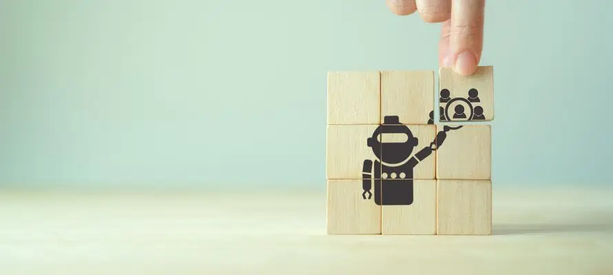 3 by 3 stack of wooden blocks with a design of a robot holding a magnifying glass over icons of people to represent HR technology trends.