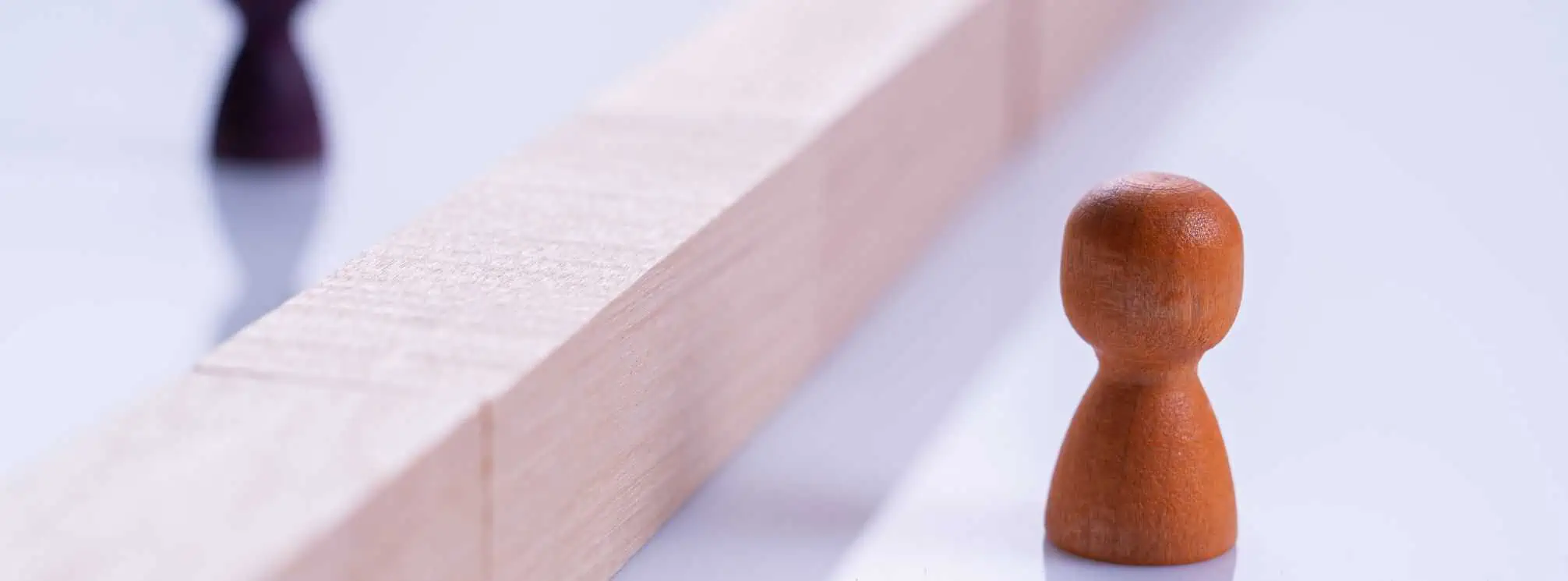 Two wooden pegs separated by a wooden block barrier to represent barriers in healthcare.