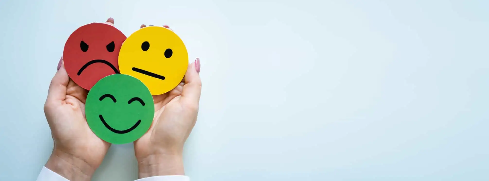 A woman's hands cupped together to hold three circular cutouts with a smiley face, neutral face, and angry face drawn on them.