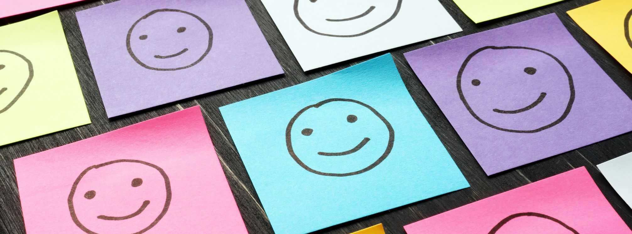 multi-color sticky notes arranged neatly on a black desk with smiley faces drawn on them