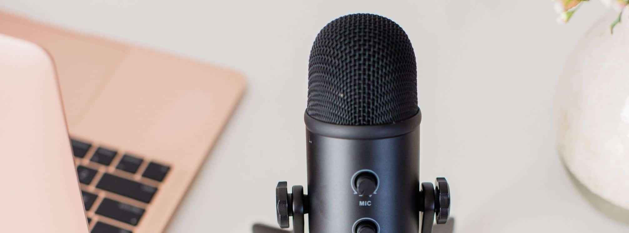 podcast microphone next to a pink Apple Macbook computer.