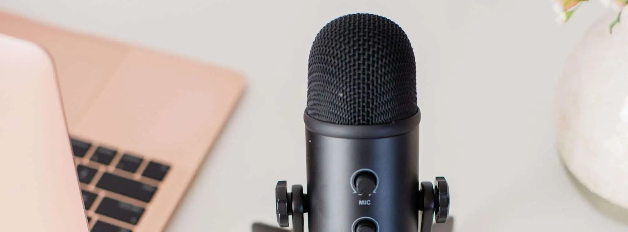 podcast microphone next to a pink Apple Macbook computer.