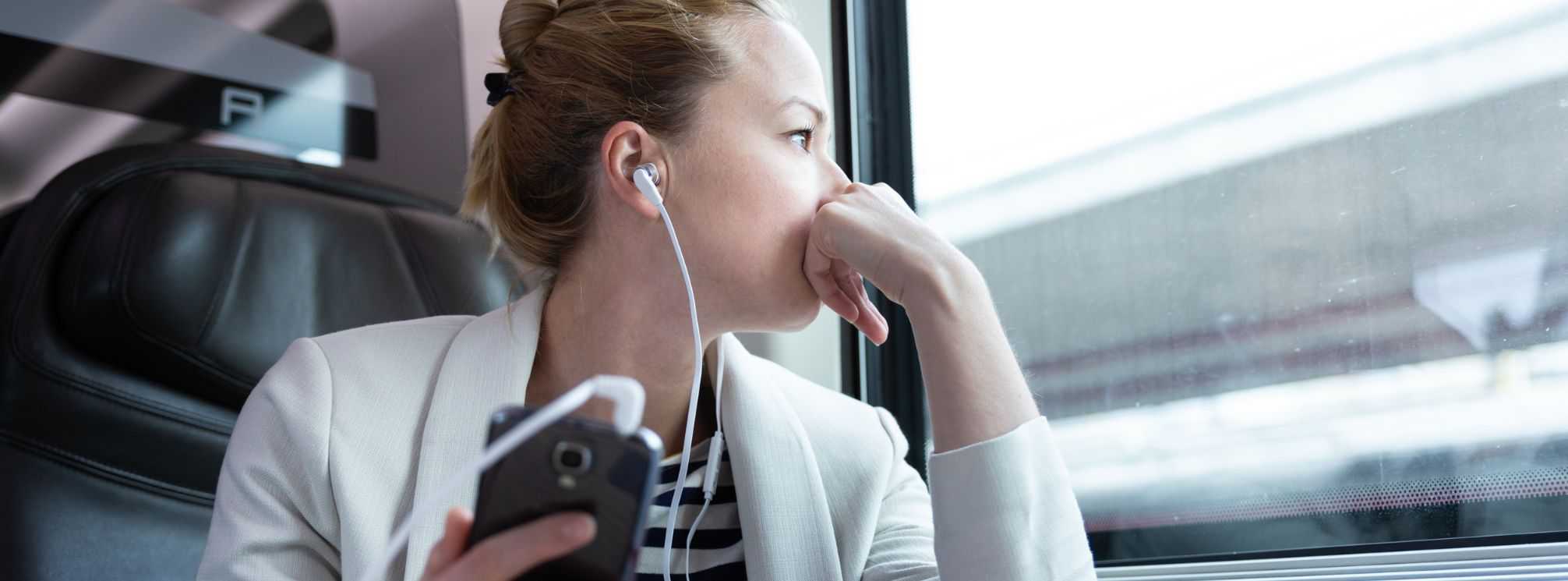 Female employee listening to a podcast while commuting to work on a train.