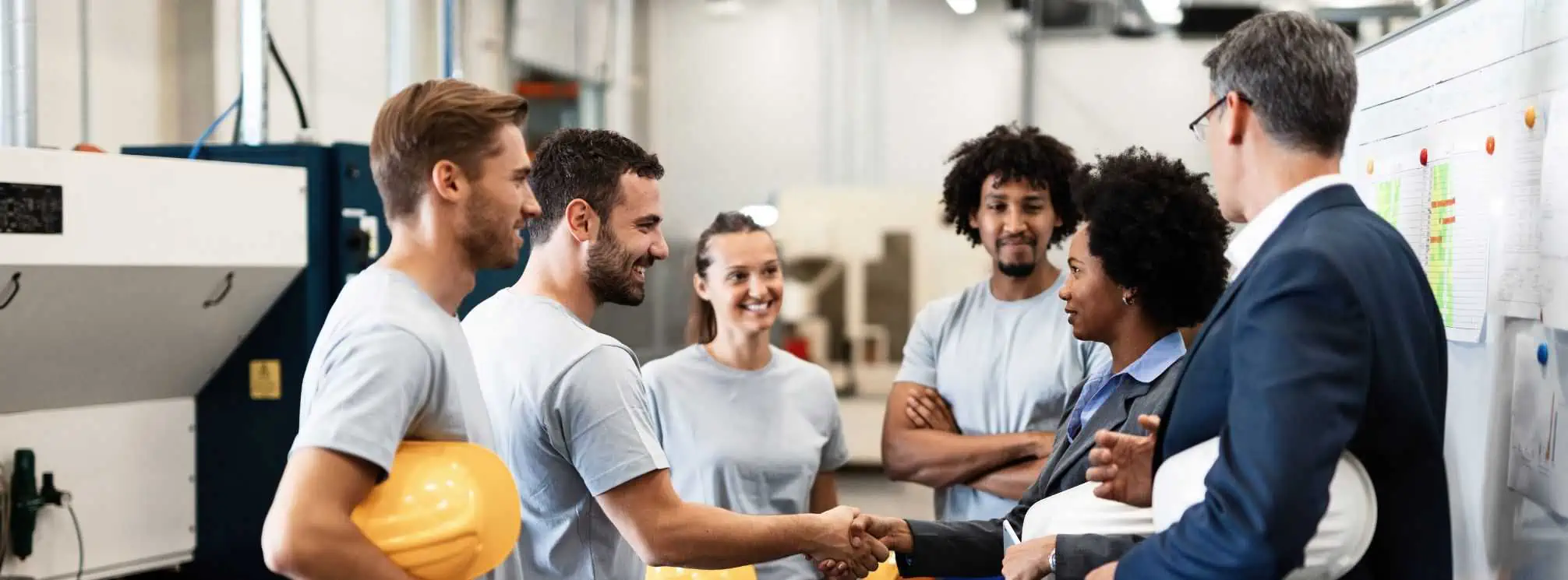 Positive work dynamic in a manufacturing environment. Group of employees all smiling. One set are shaking hands.