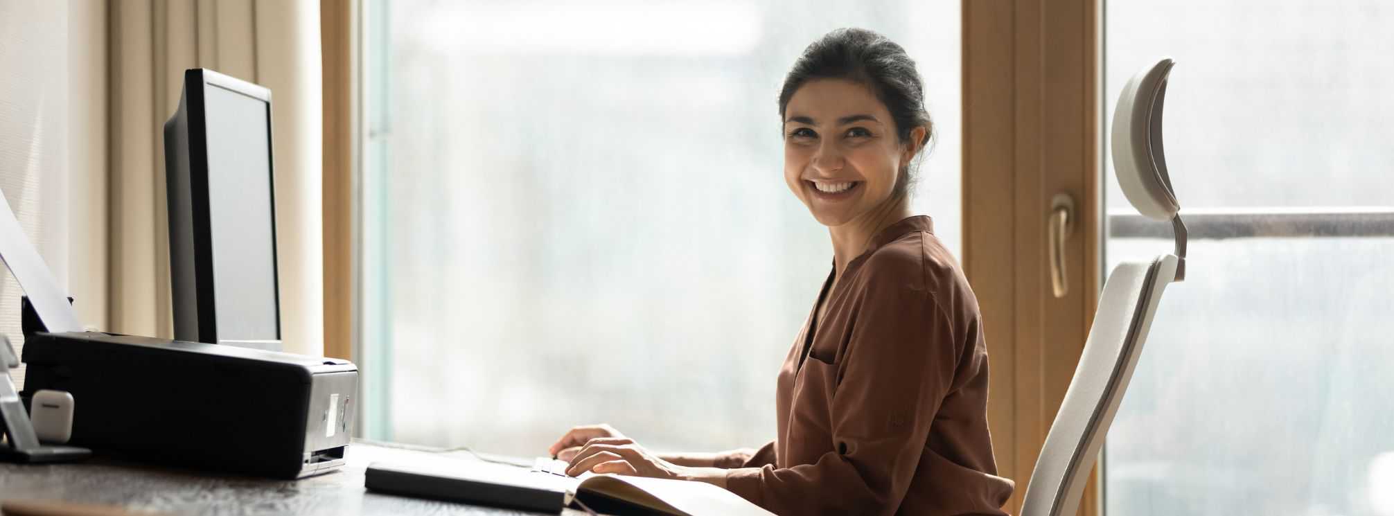 Smiling, happy female employee sitting at her desk and looking at the camera.