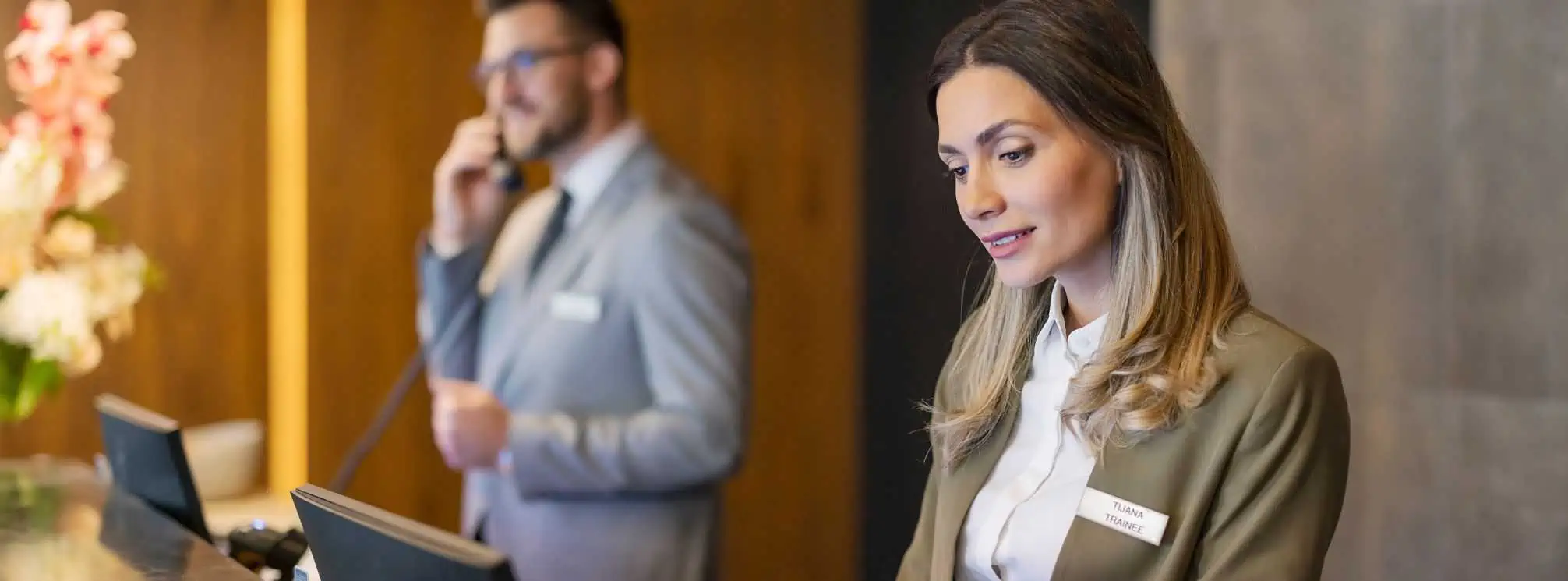 Two hotel employees working at the front desk, communicating with customers on the phone.