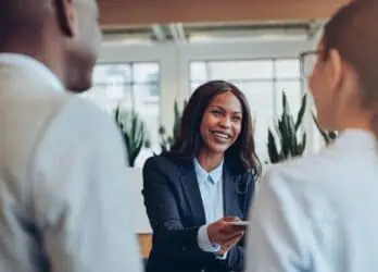 Hospitality employee greeting two guests at the hotel front desk.